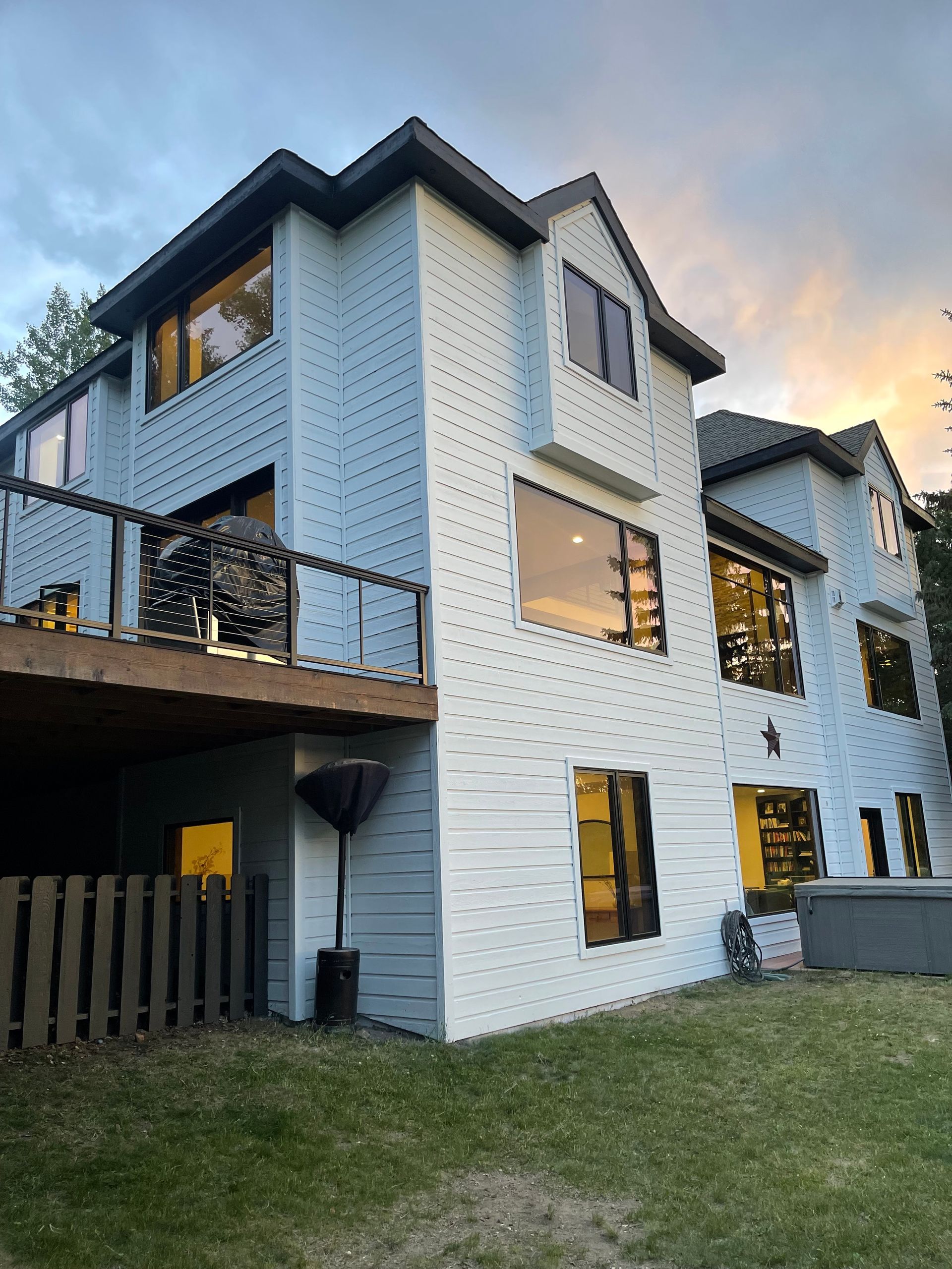Two-story light blue house with multiple large windows, a deck, and a fenced yard.