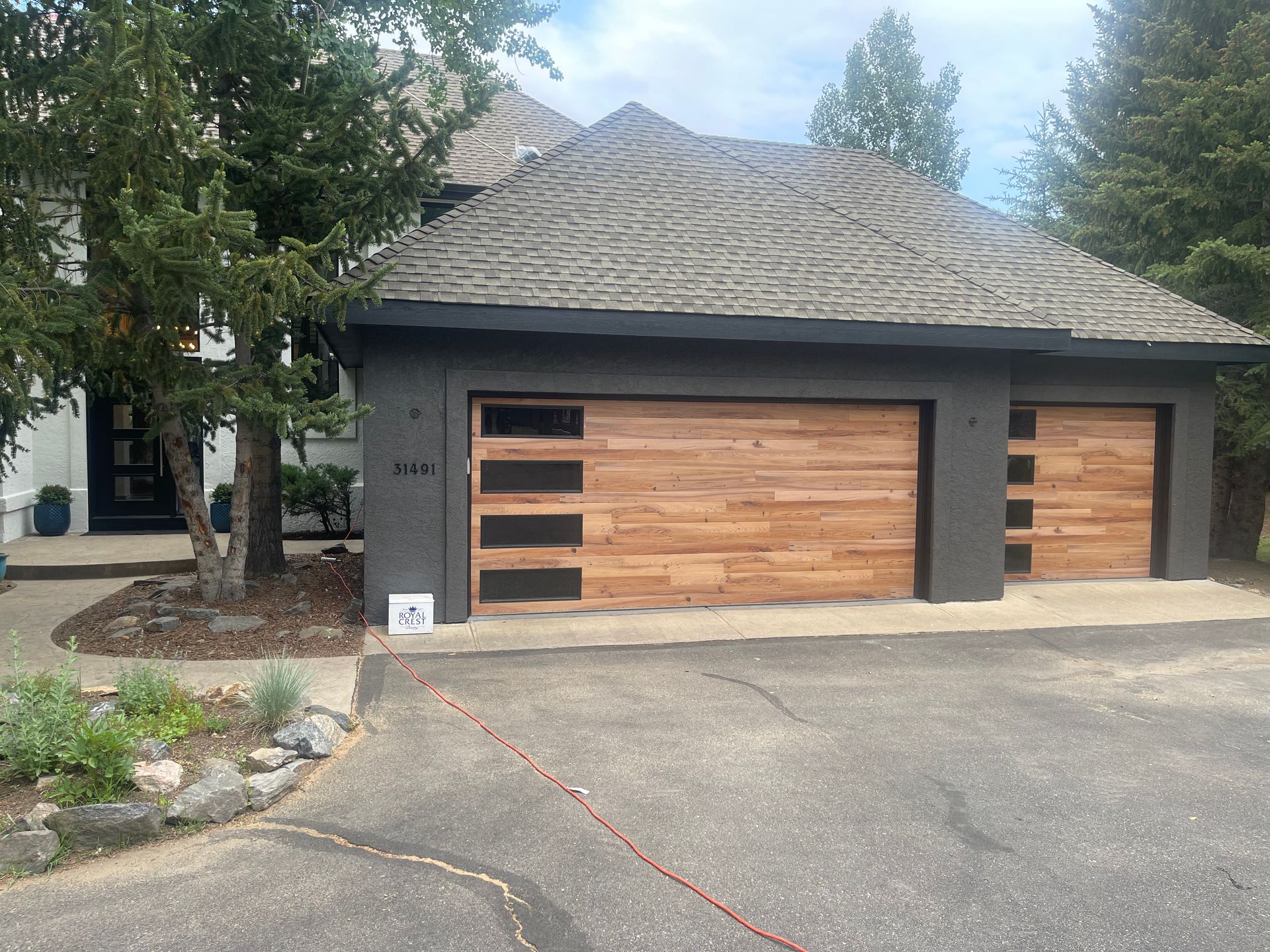 Brown wooden garage doors with glass panels on a dark gray house with a textured roof.