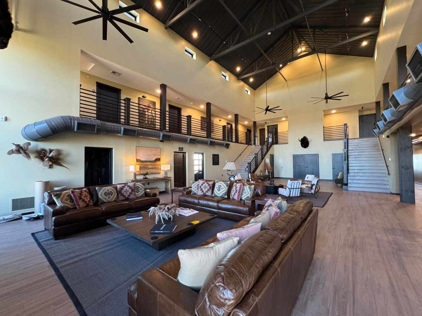 Modern living room with brown leather sofas, high ceilings, and a staircase in a spacious open-concept home