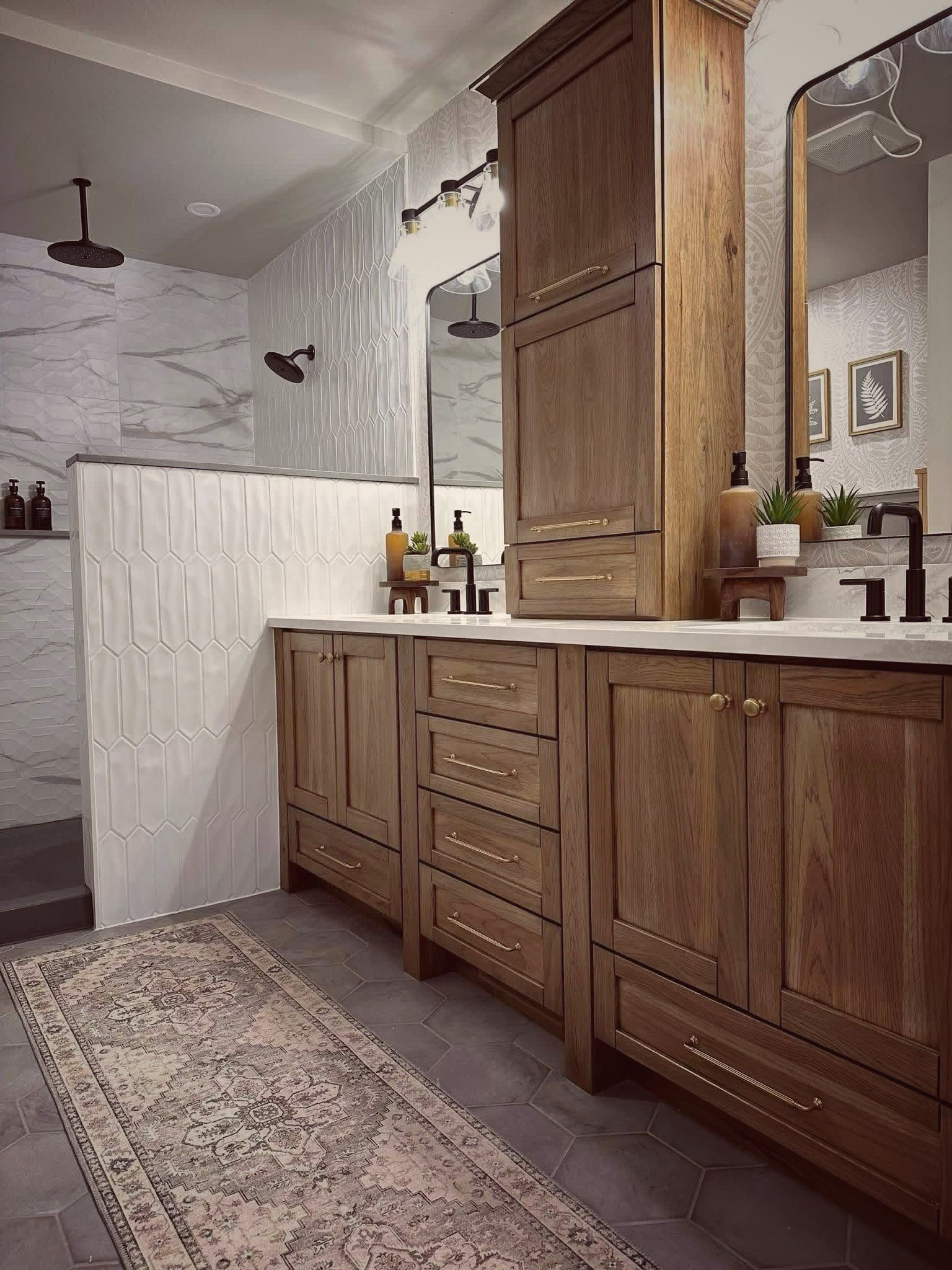 Warm bathroom with wood vanity, marble-pattern shower, and patterned rug.