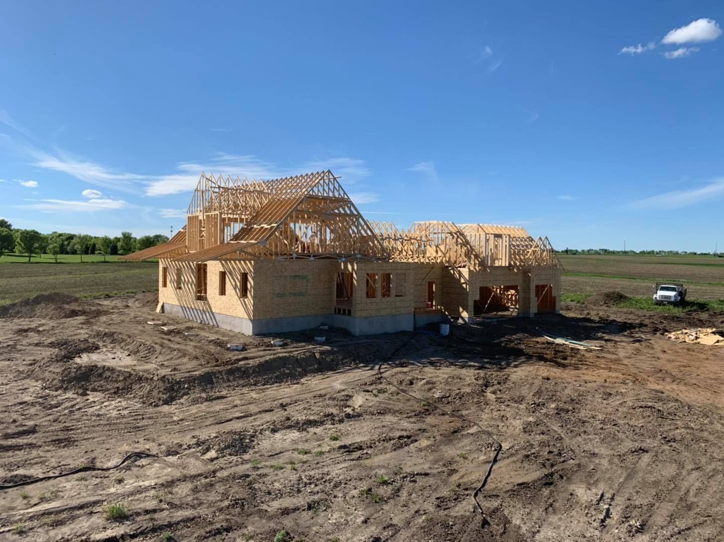 House under construction with wooden framing on a dirt lot under a clear blue sky