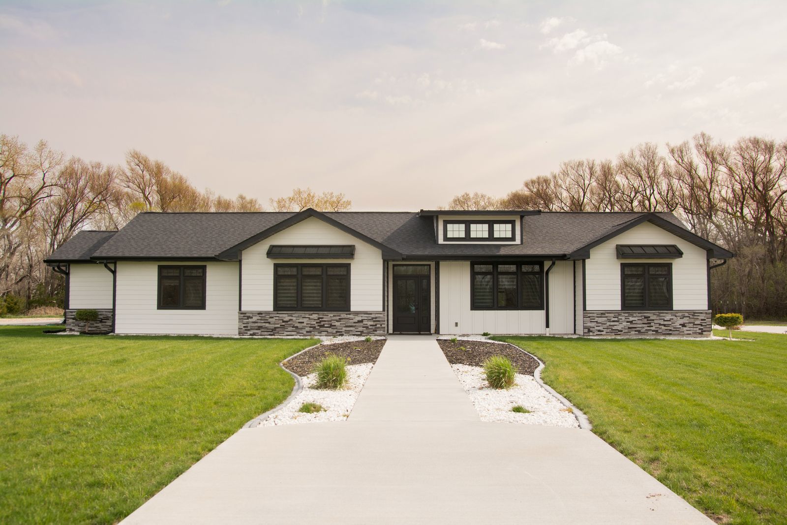 Modern single-story house with stone and white exterior, front walkway, and large green lawn