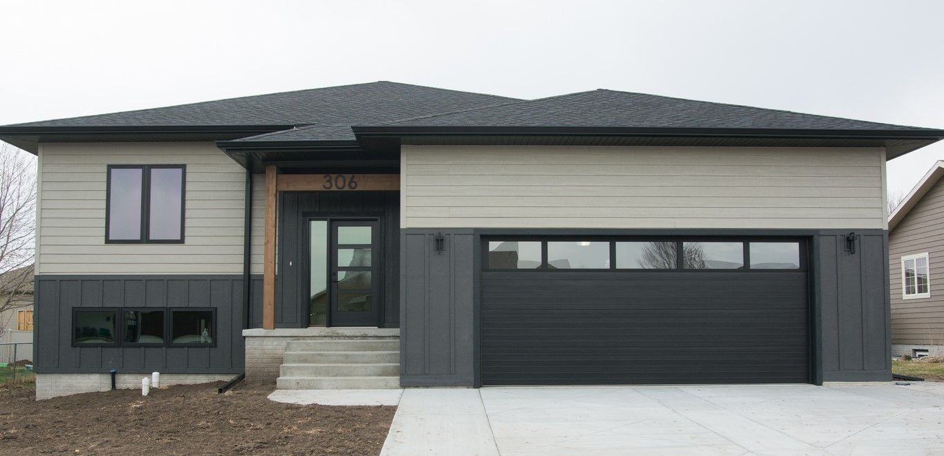 Modern two-story house exterior with gray siding, black garage door, and front steps