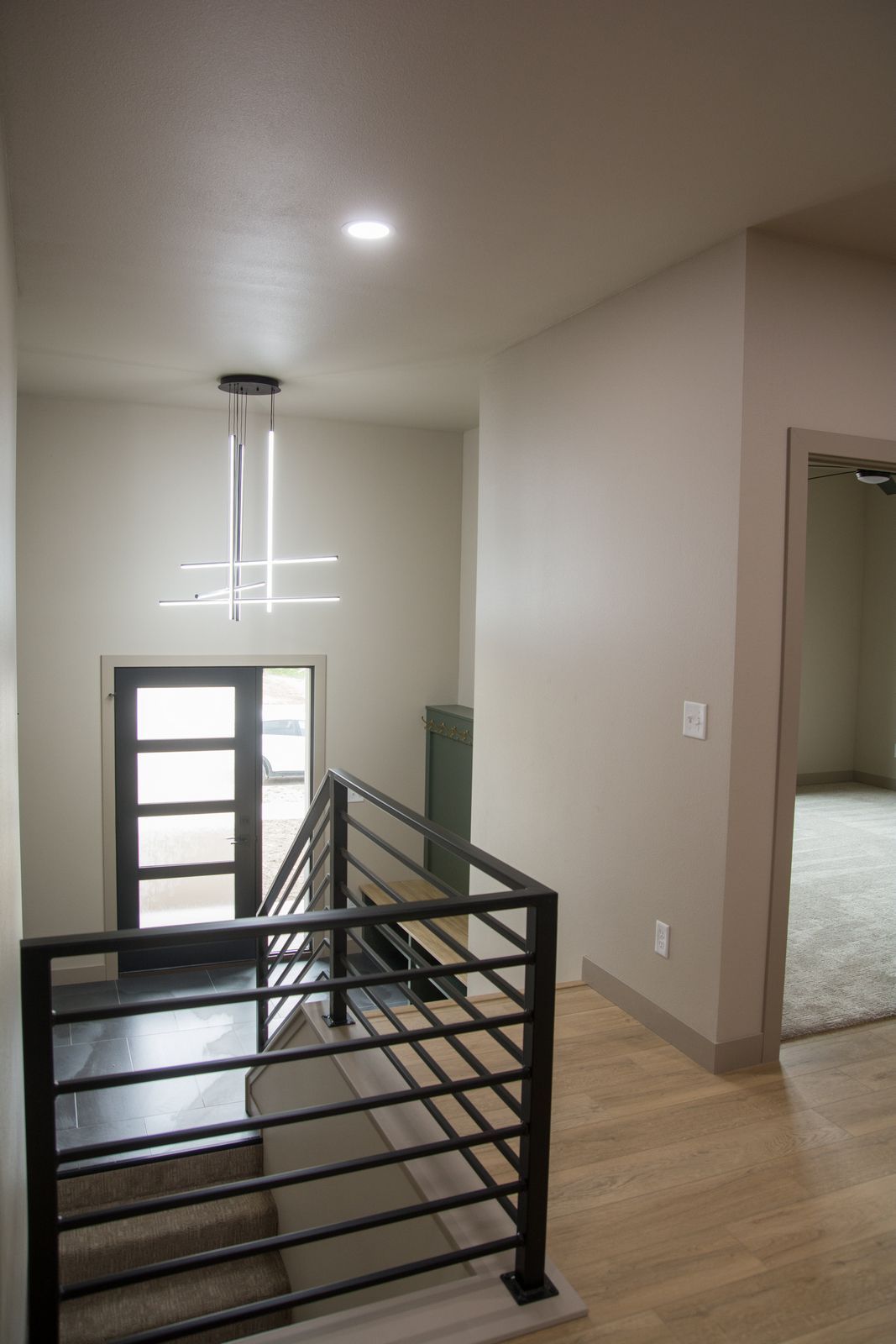 Stair landing with black metal railing, wood floor, white walls, and a doorway to a carpeted room