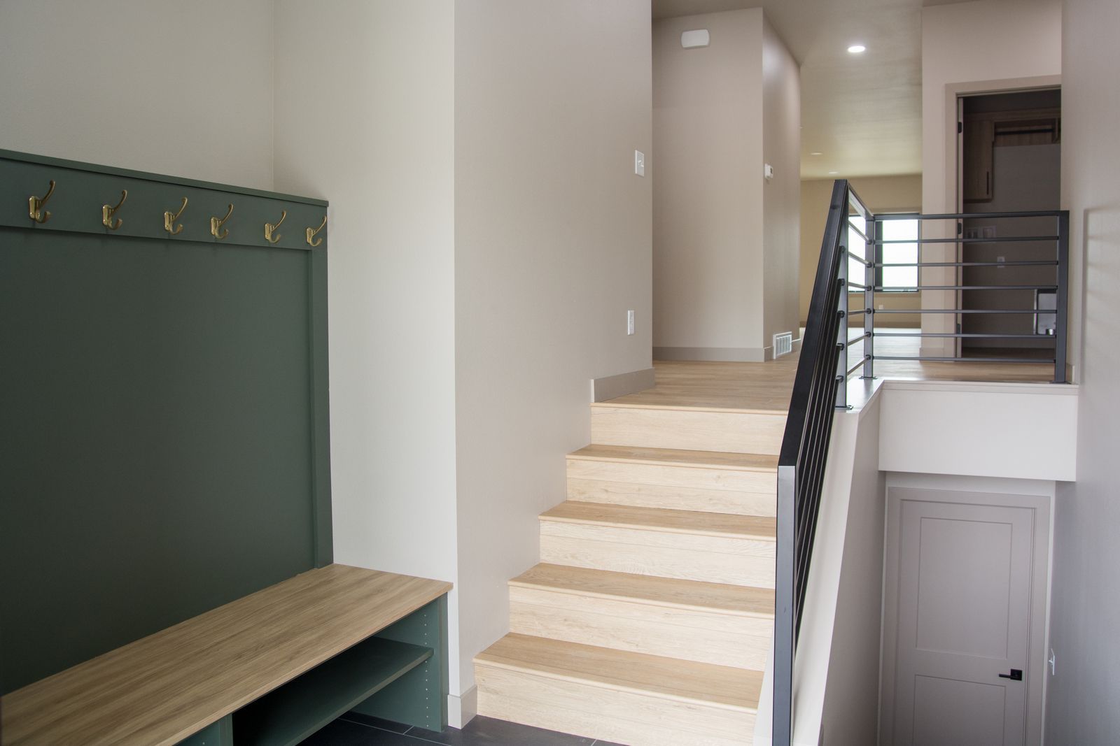 Modern entryway with stairs, green bench and wall hooks, and a railing overlooking a lower level
