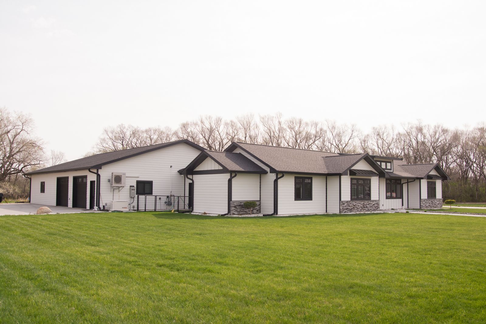 Single-story white house with dark trim on a large green lawn under an overcast sky