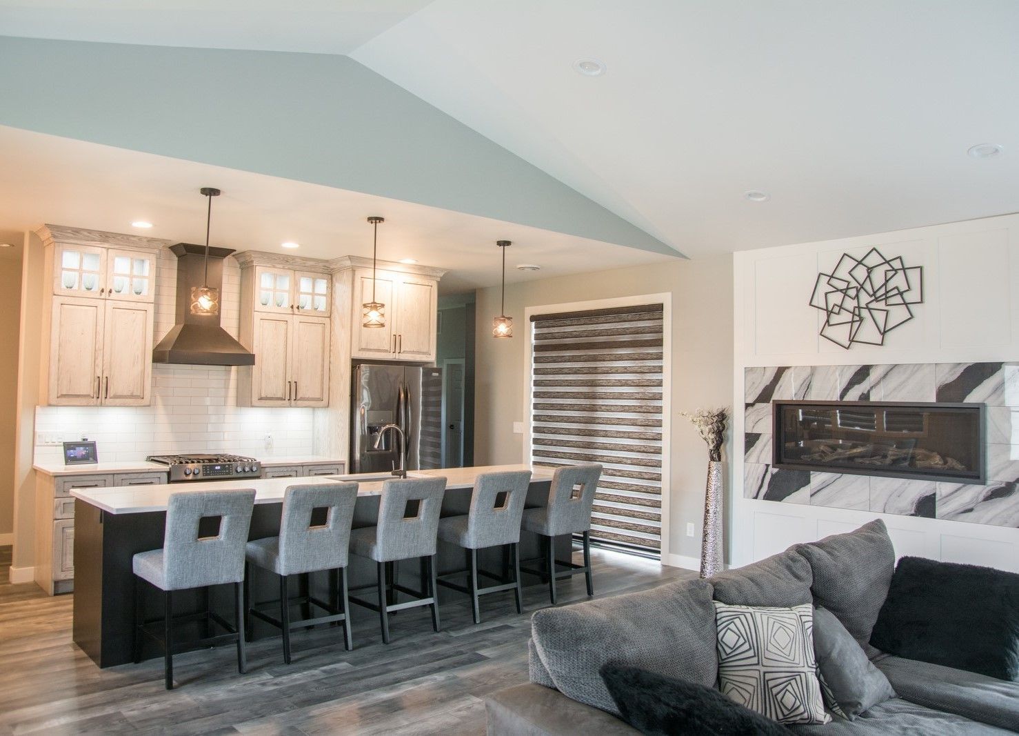 Open-concept kitchen and living room with gray sectional, island stools, and fireplace