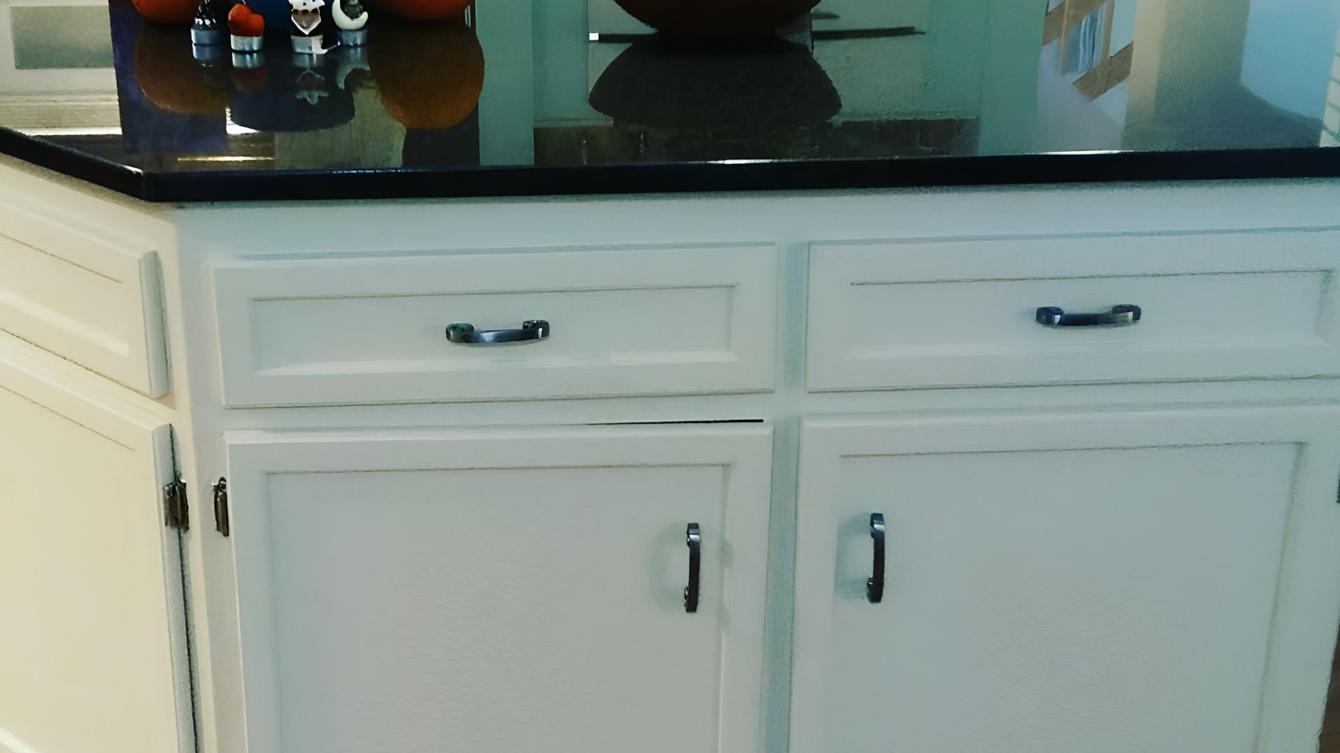 White kitchen cabinets with black handles beneath a dark countertop.