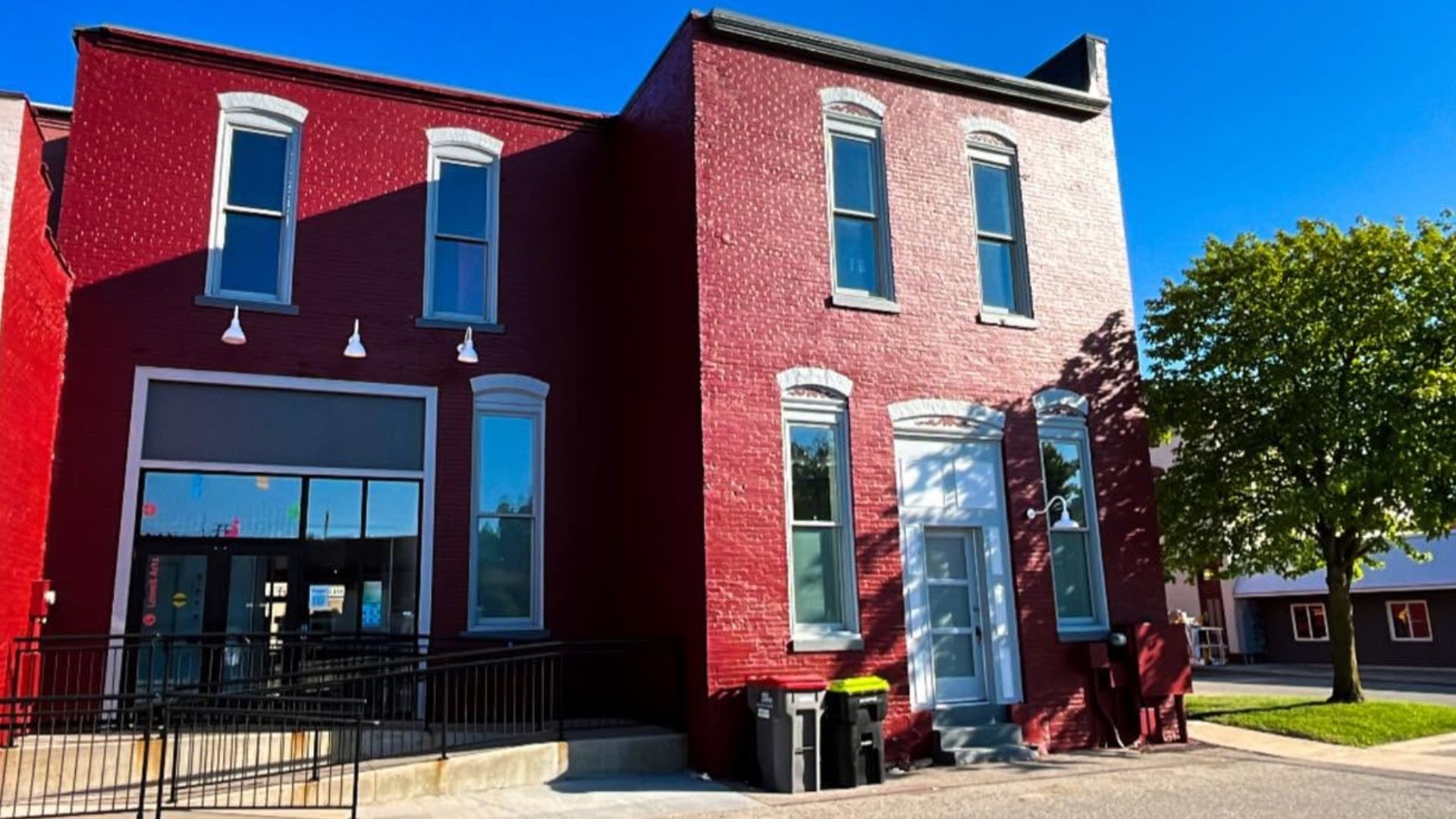 Two red brick buildings with large windows on a sunny street corner