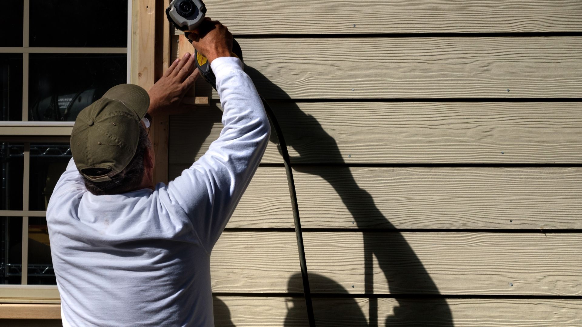 Person using a power drill to fasten horizontal siding on a house exterior.