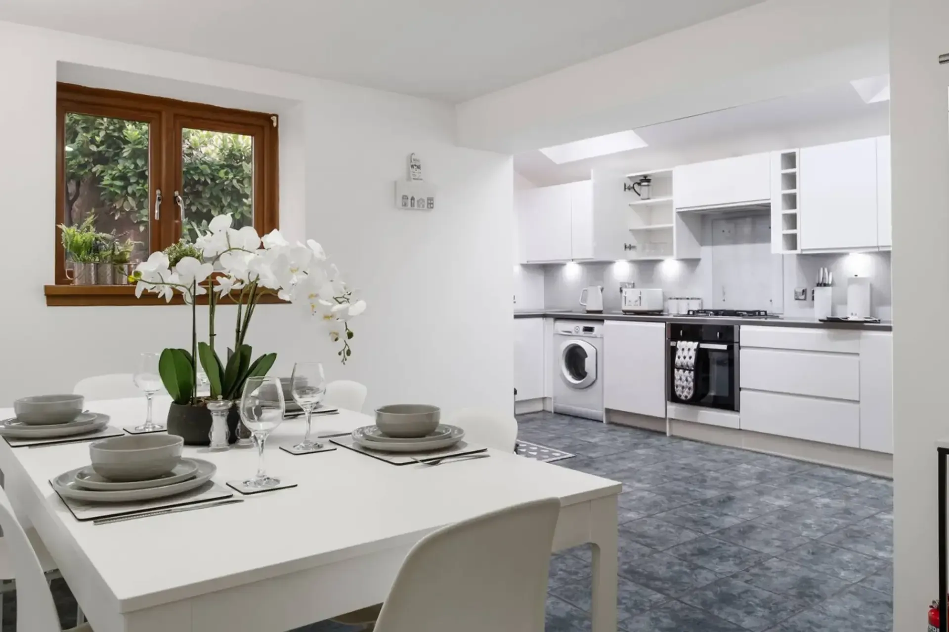 Bright white dining room opening to a modern white kitchen with gray carpet and table set for four.