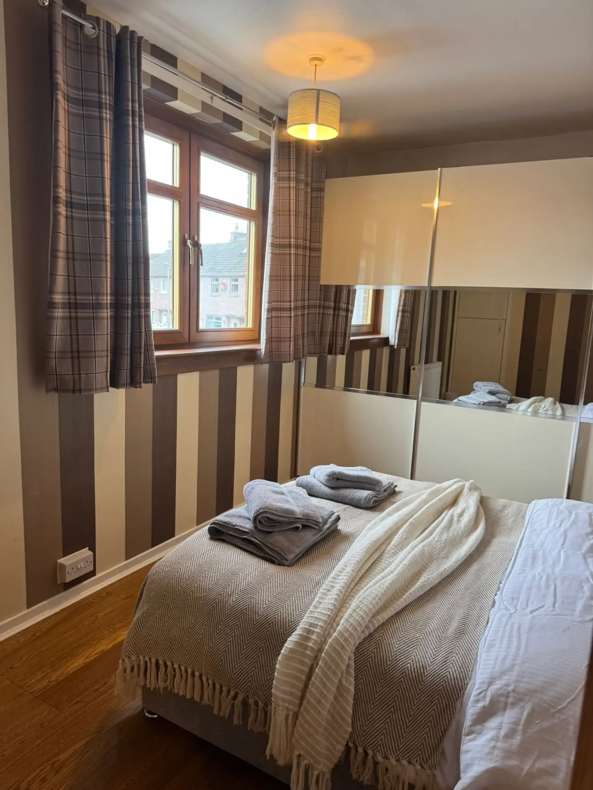 Cozy bedroom with striped walls, window, mirror wardrobe, and a neatly made bed with folded towels