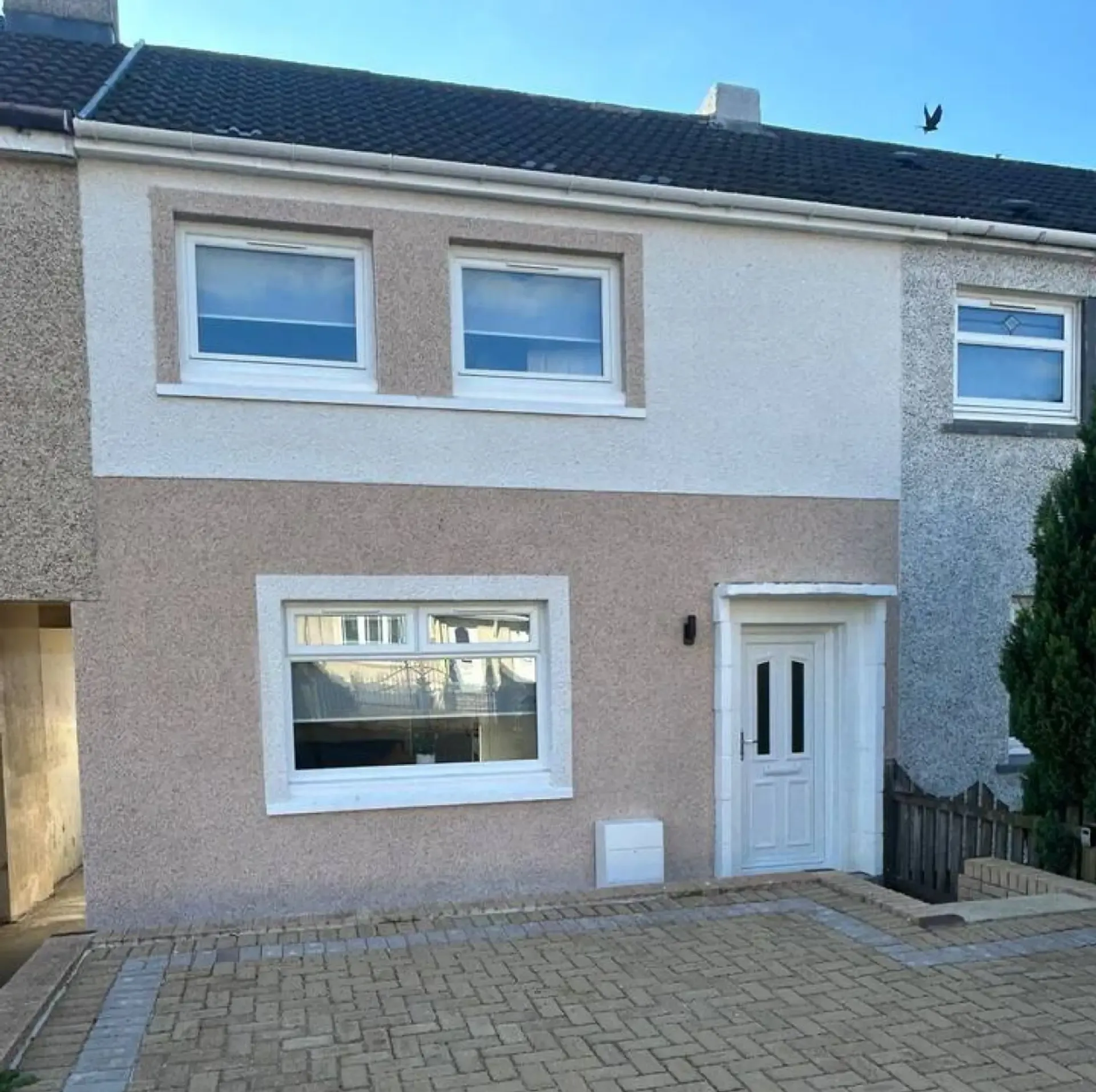 Modern two-story townhouse with beige stucco, white trim, front door, and paved driveway