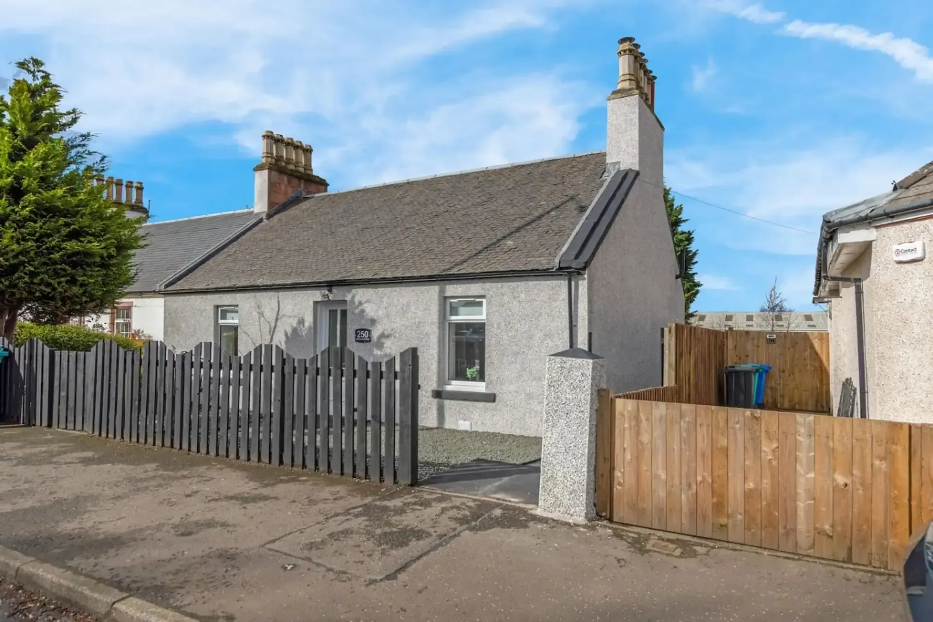 Gray cottage with fenced front yard and wooden gate on a quiet street