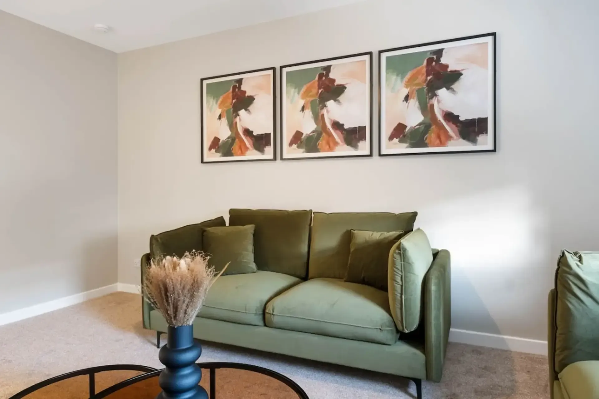 Minimalist living room with green sofa, framed wall art, and a round coffee table with dried flowers