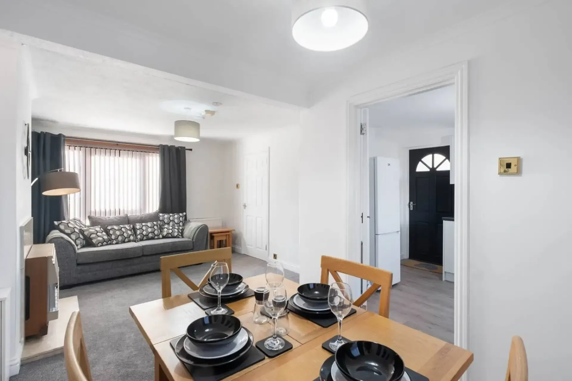 Bright dining area with set table, gray sofa, and hallway in a small modern apartment