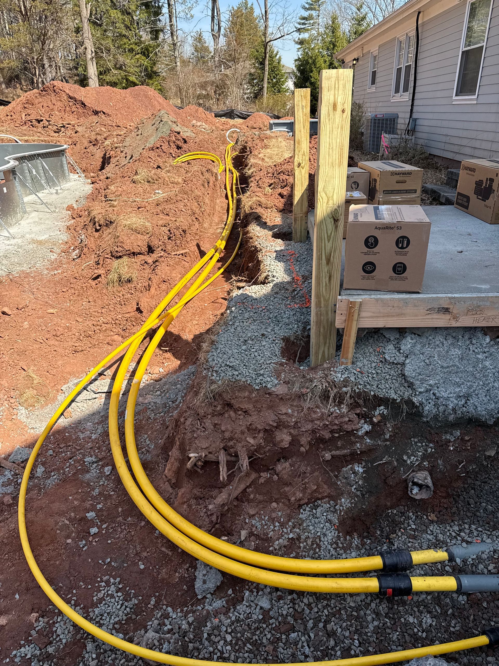 Yellow gas lines running through a trench, near a wooden fence and building.