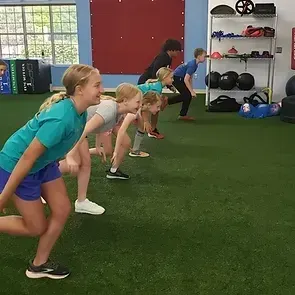 A group of children are doing squats in a gym.