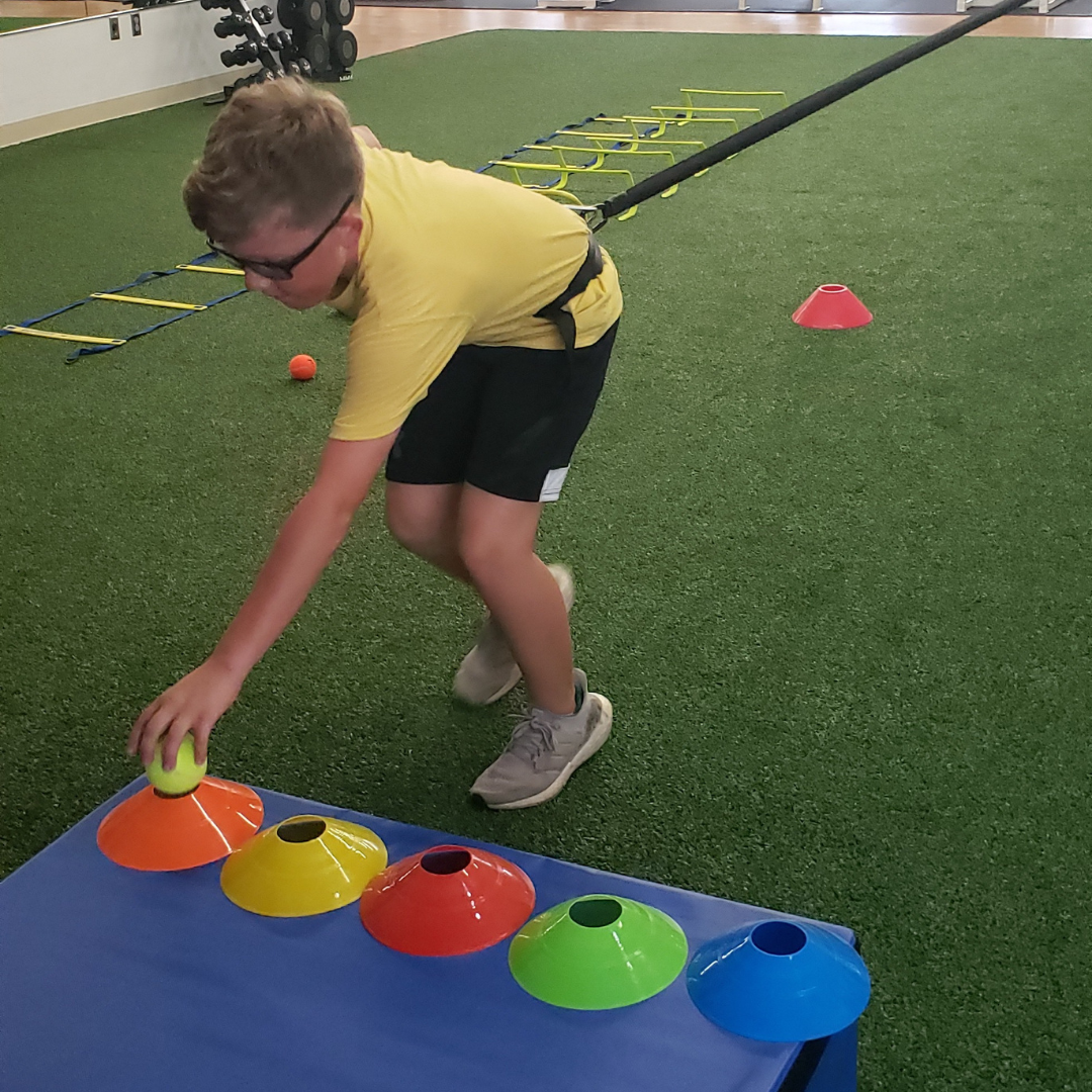 A boy in a yellow shirt is reaching for a tennis ball