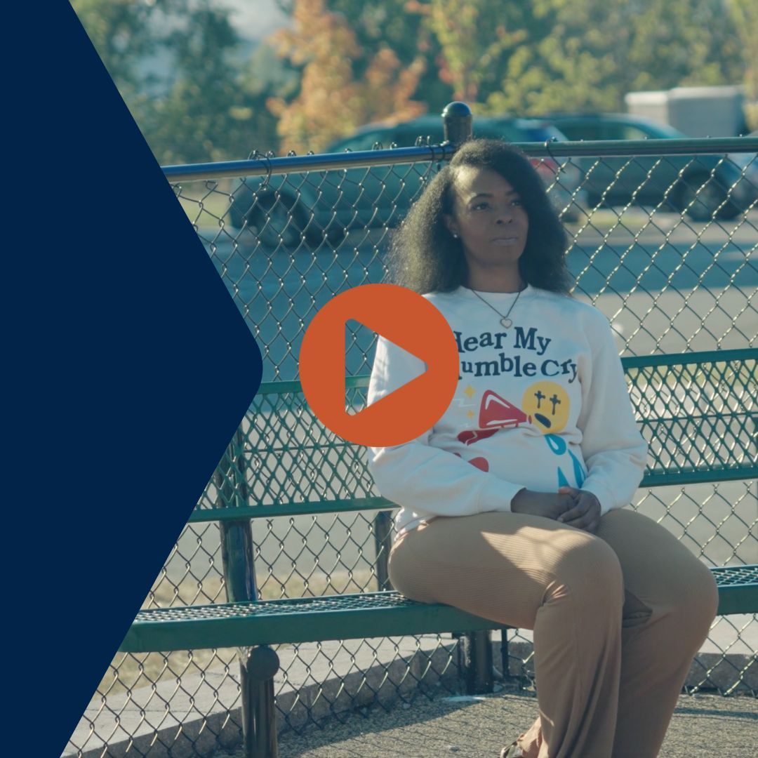 Woman sits on a park bench wearing a white sweatshirt with colorful emojis, sunny day.