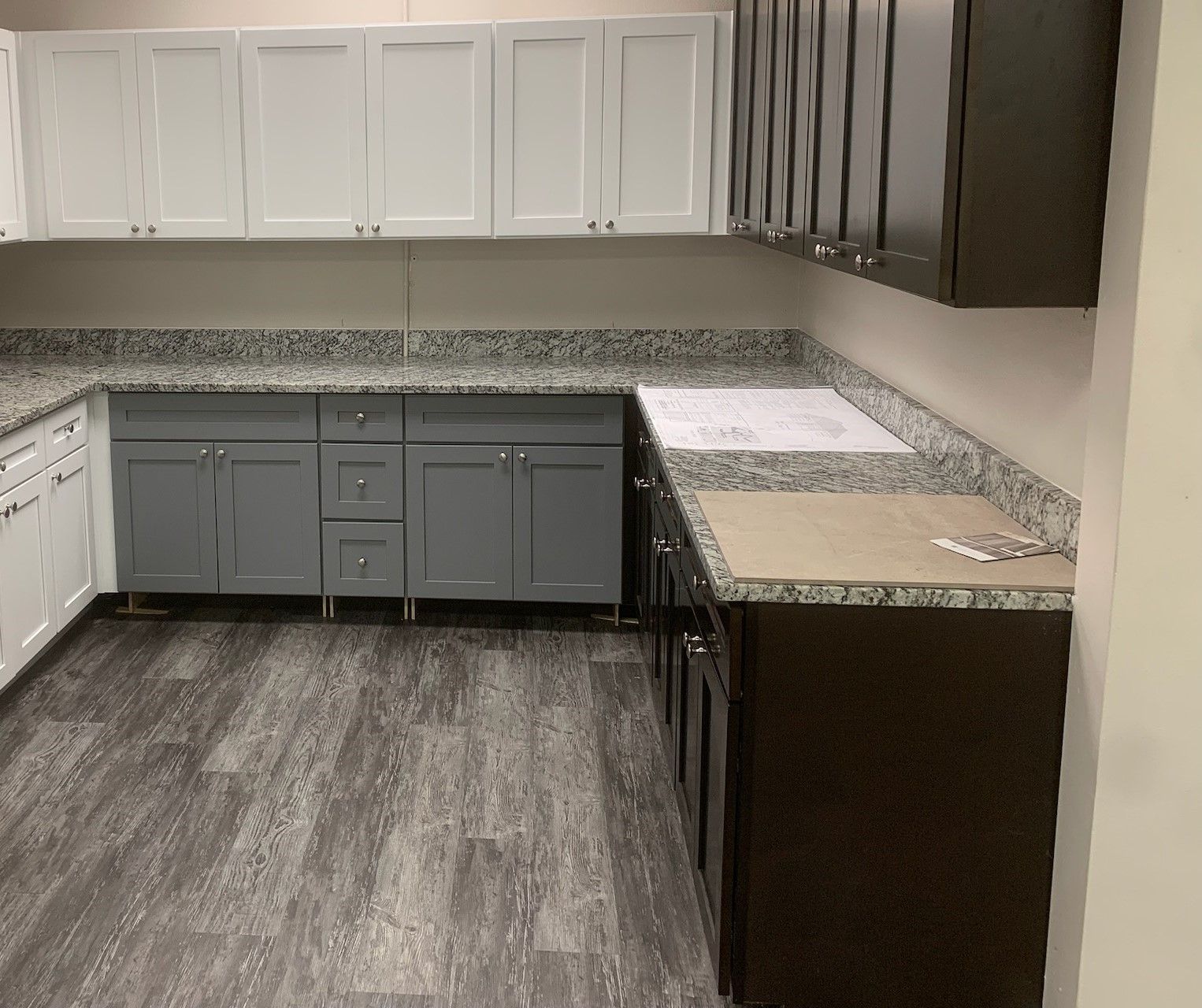 L-shaped kitchen with white, gray, and brown cabinets, speckled countertops, and gray flooring.