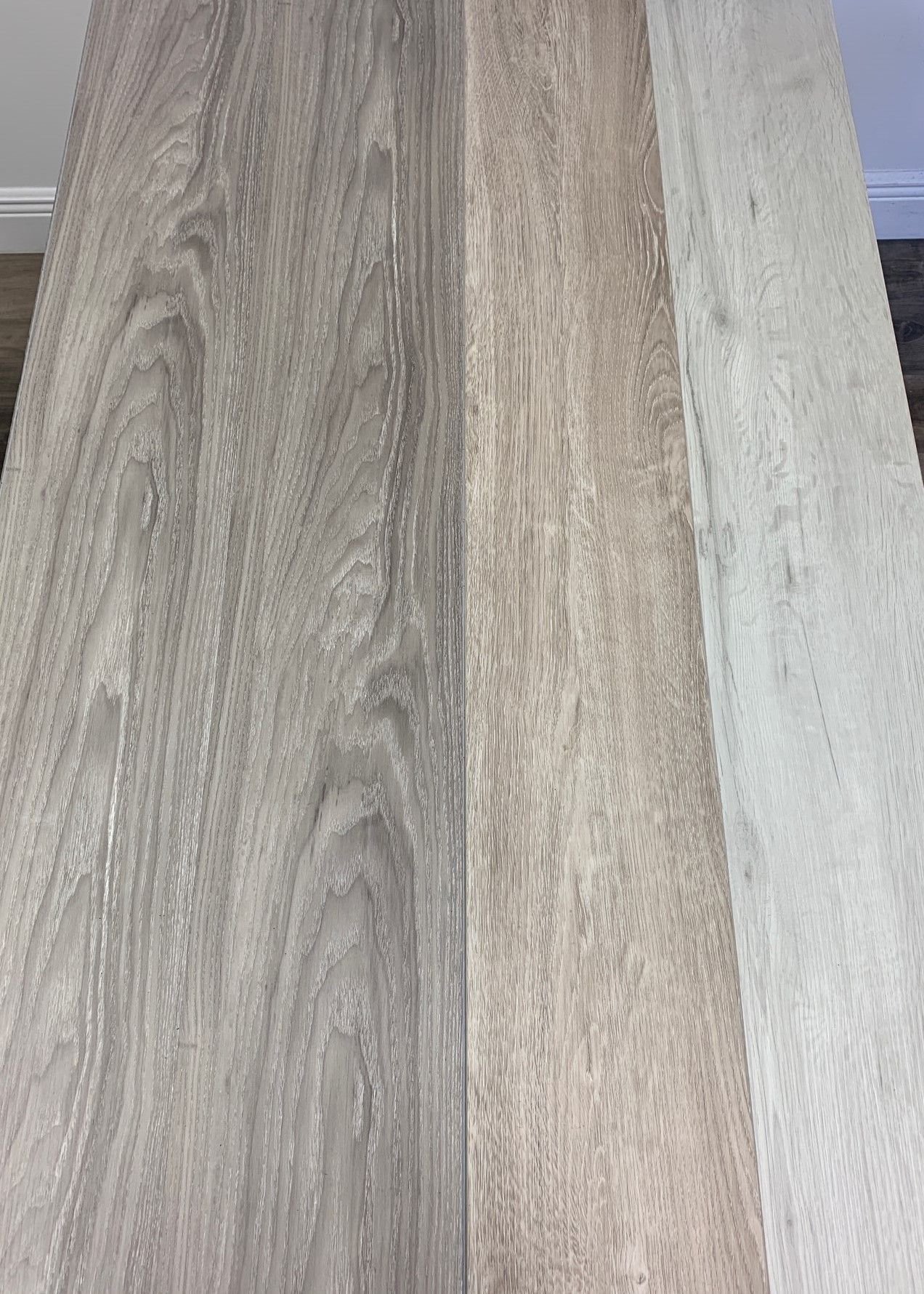 Four planks of wood flooring samples in shades of grey and beige.