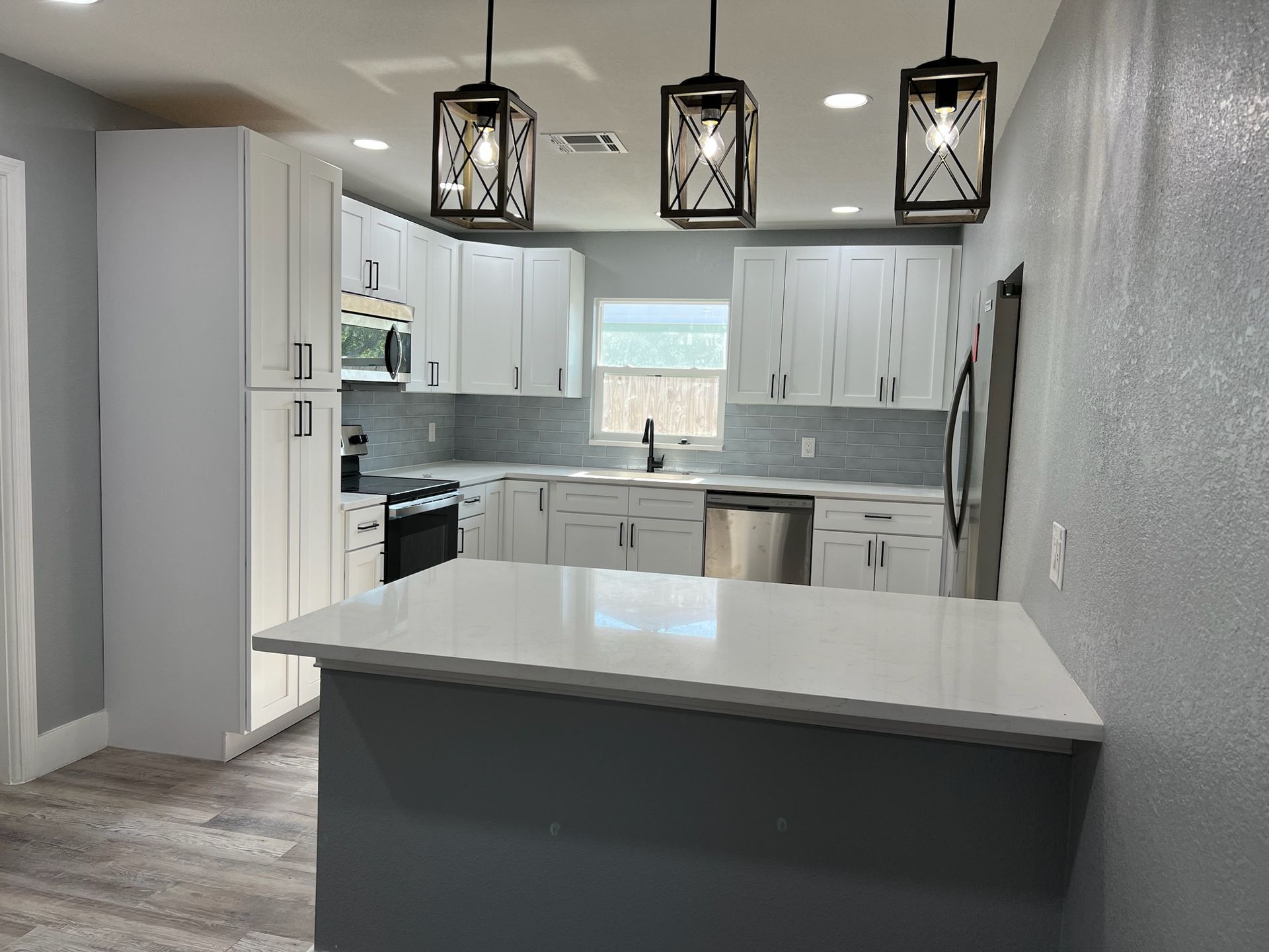 Modern kitchen with white cabinets, gray island, stainless steel appliances, and geometric pendant lights.