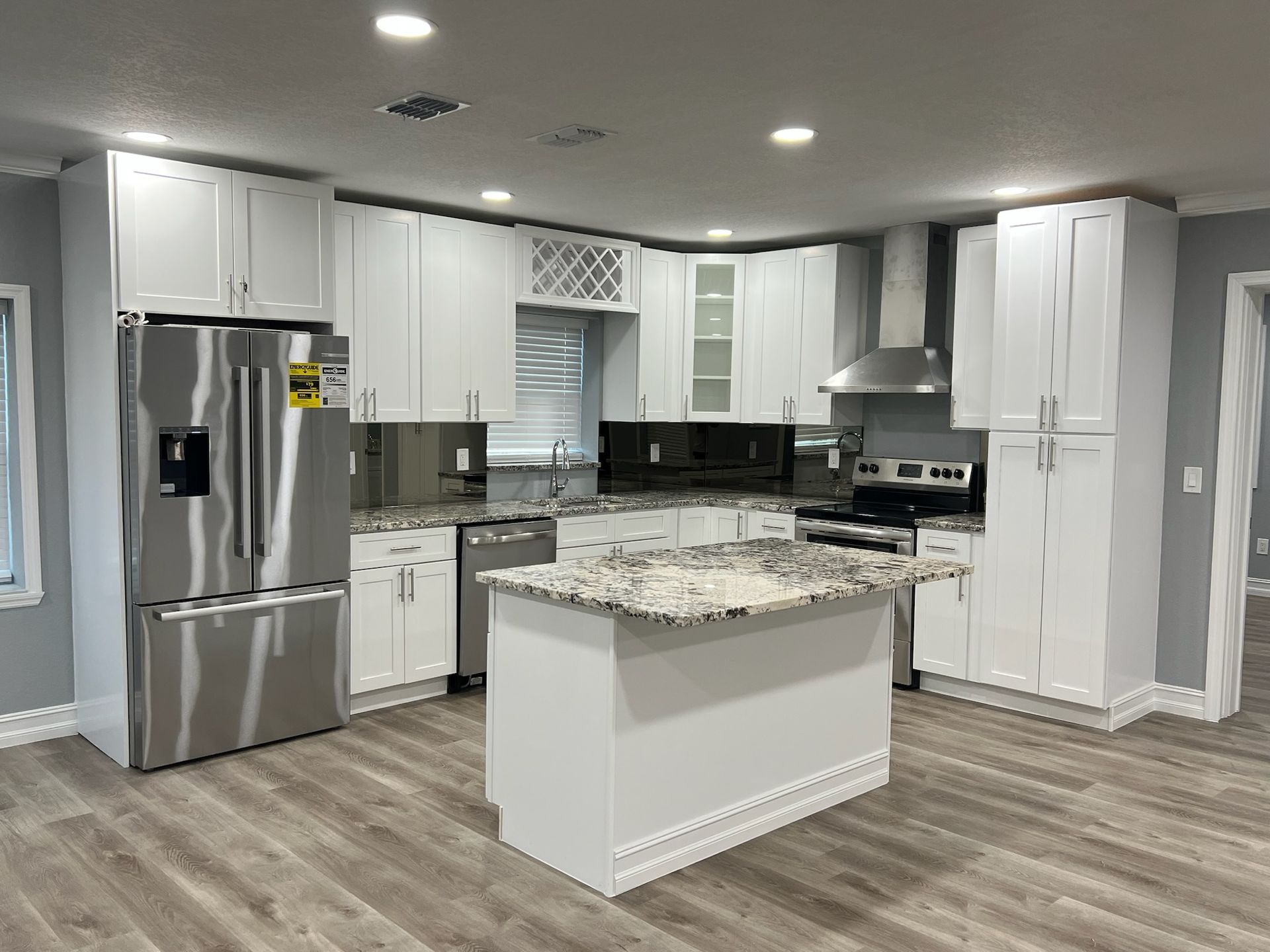 Modern white kitchen with stainless steel appliances, granite countertops, and an island.