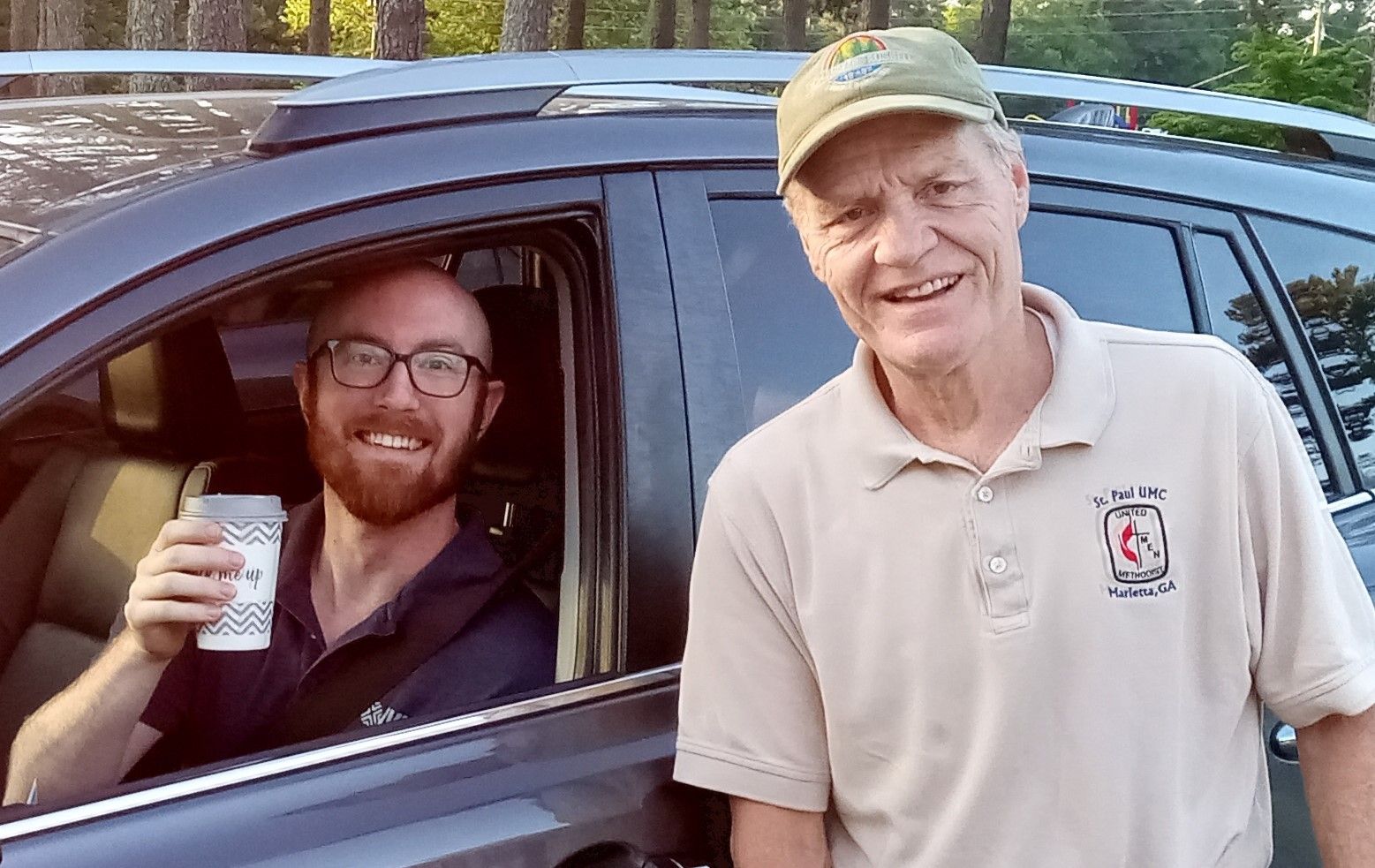 Two men are standing next to each other in front of a car.