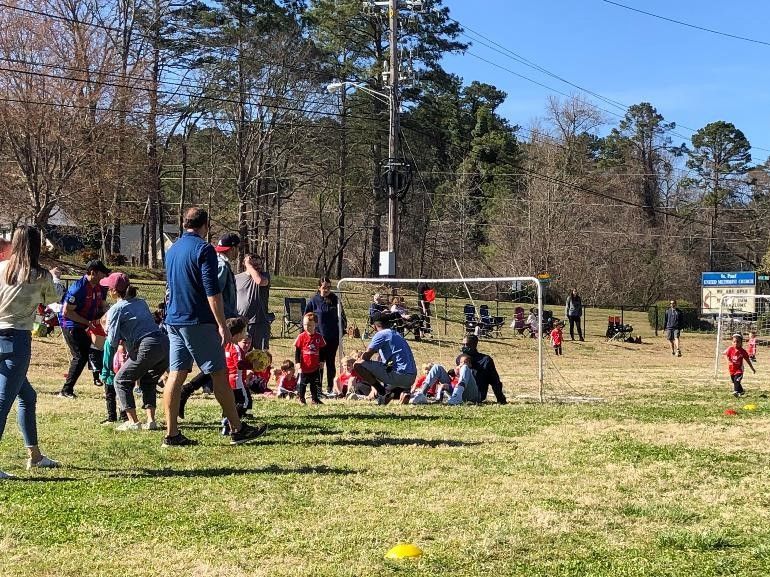 Children and adults playing soccer in a field.