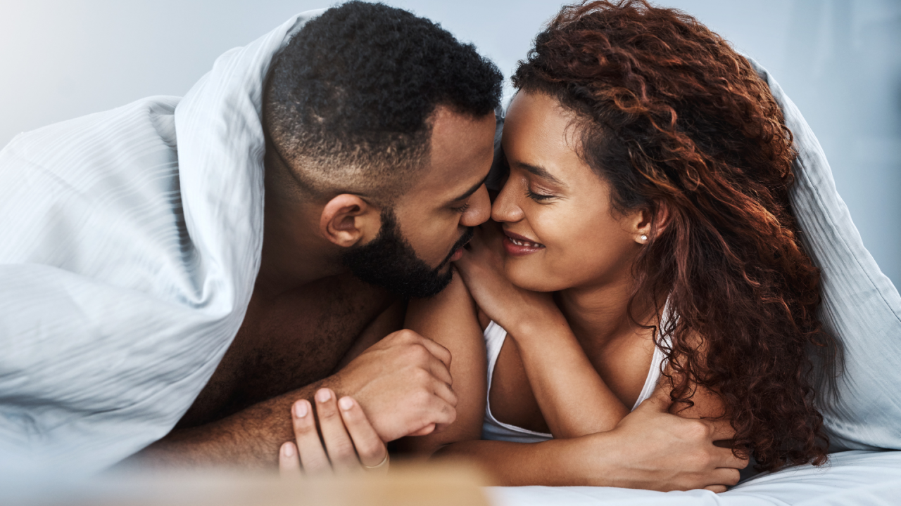 a man and a woman are laying on a bed under a blanket .