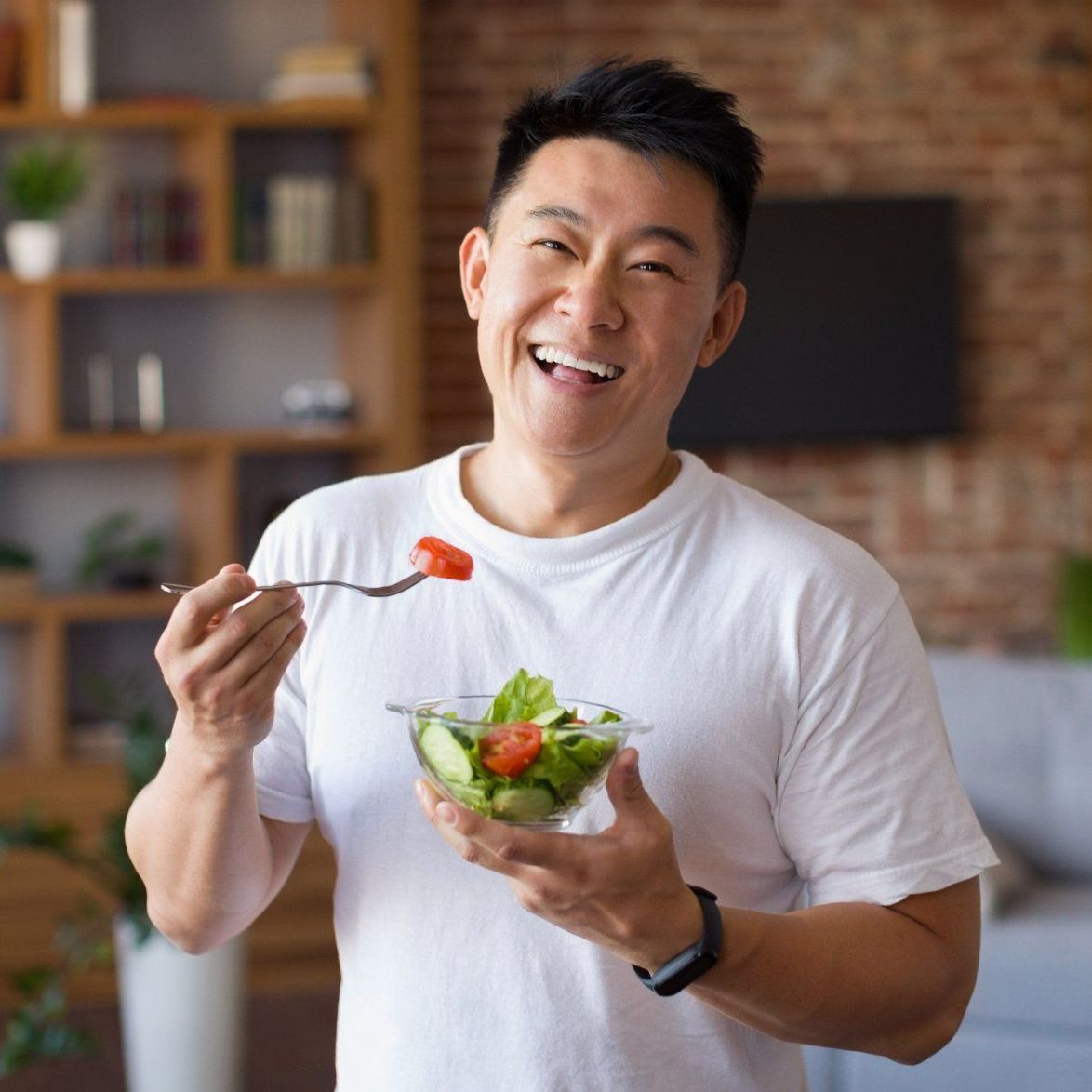 A man is eating a salad with a fork and smiling.