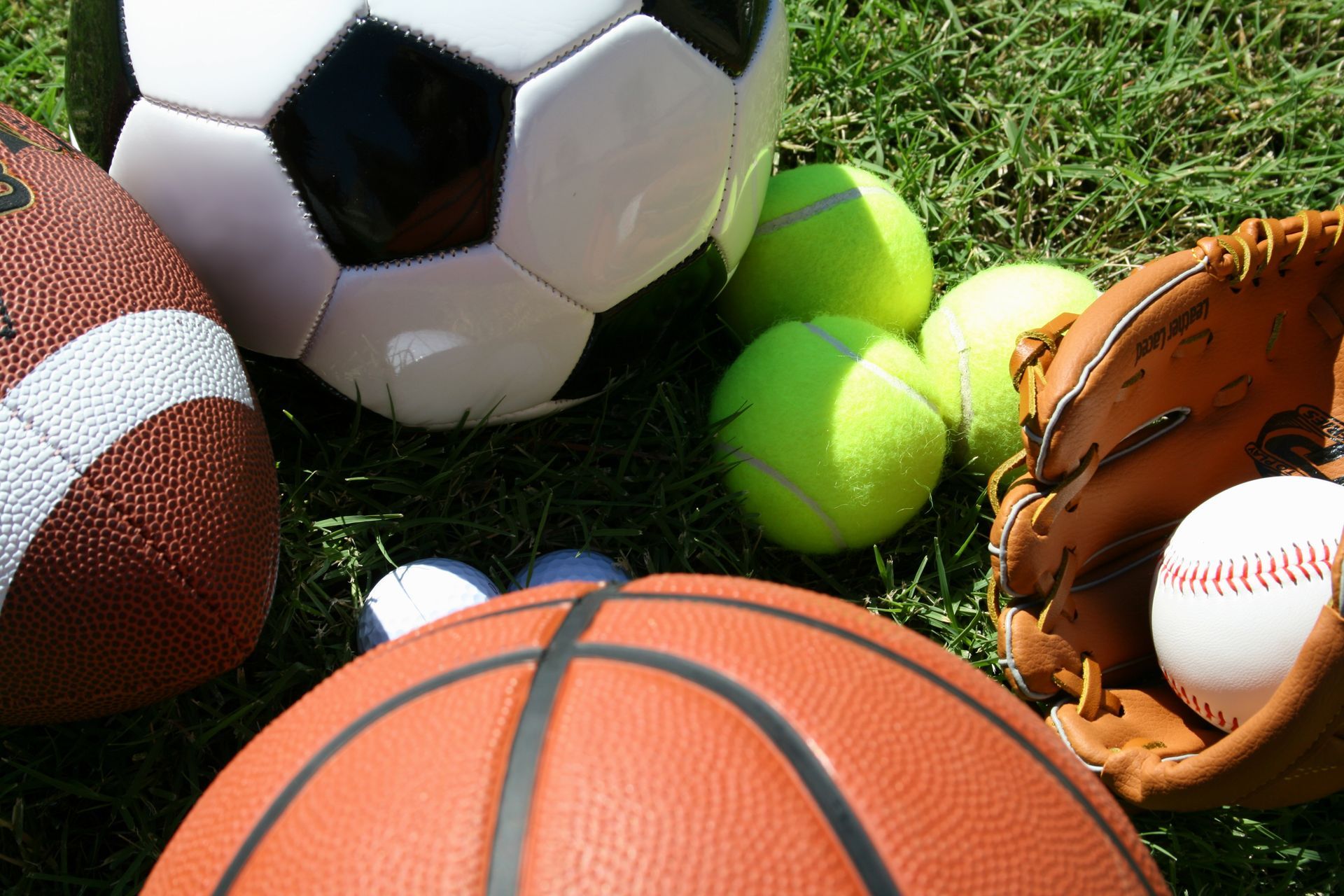 A basketball a soccer ball tennis balls and a baseball glove on the grass
