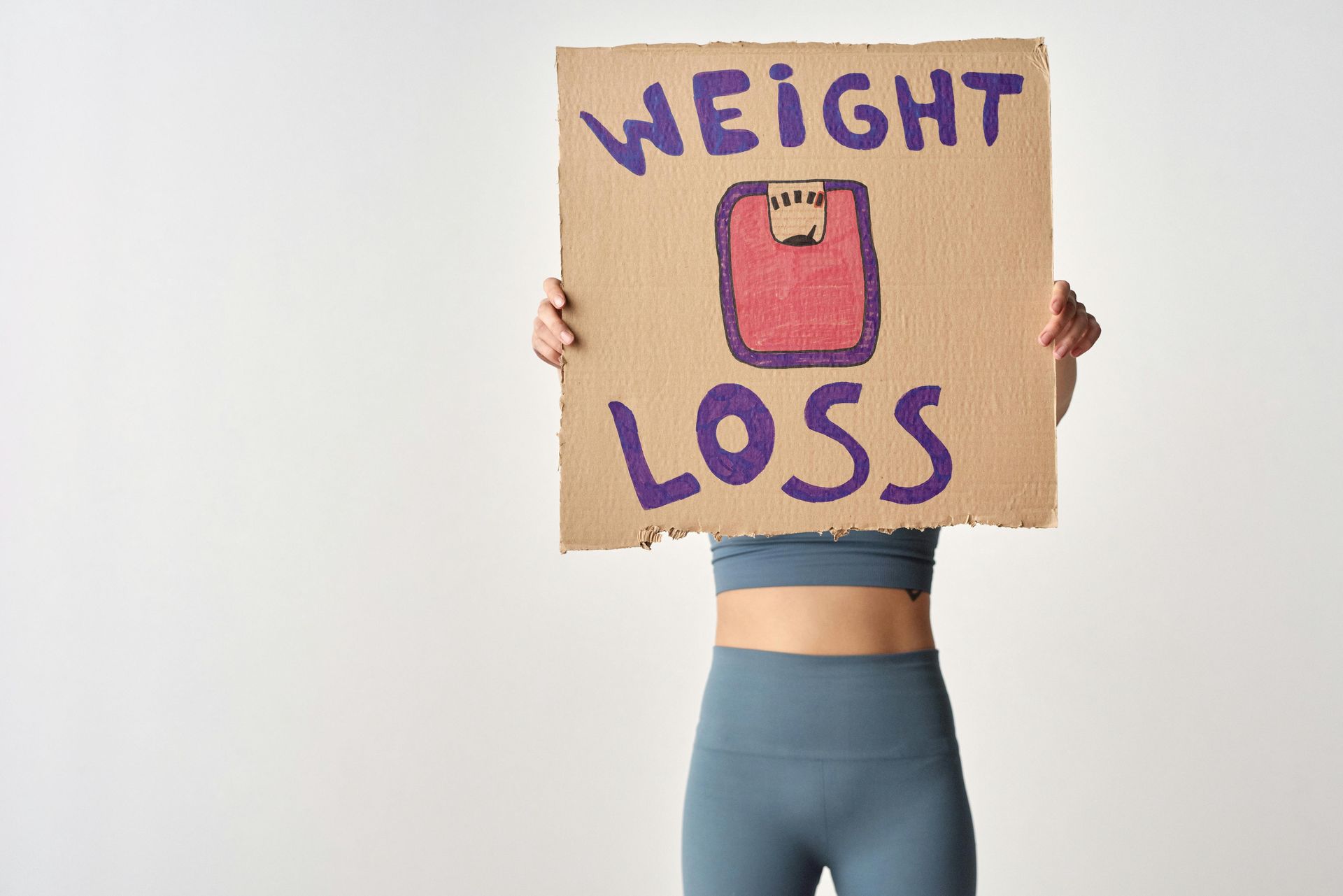 A person in blue activewear holds a piece of cardboard that reads 