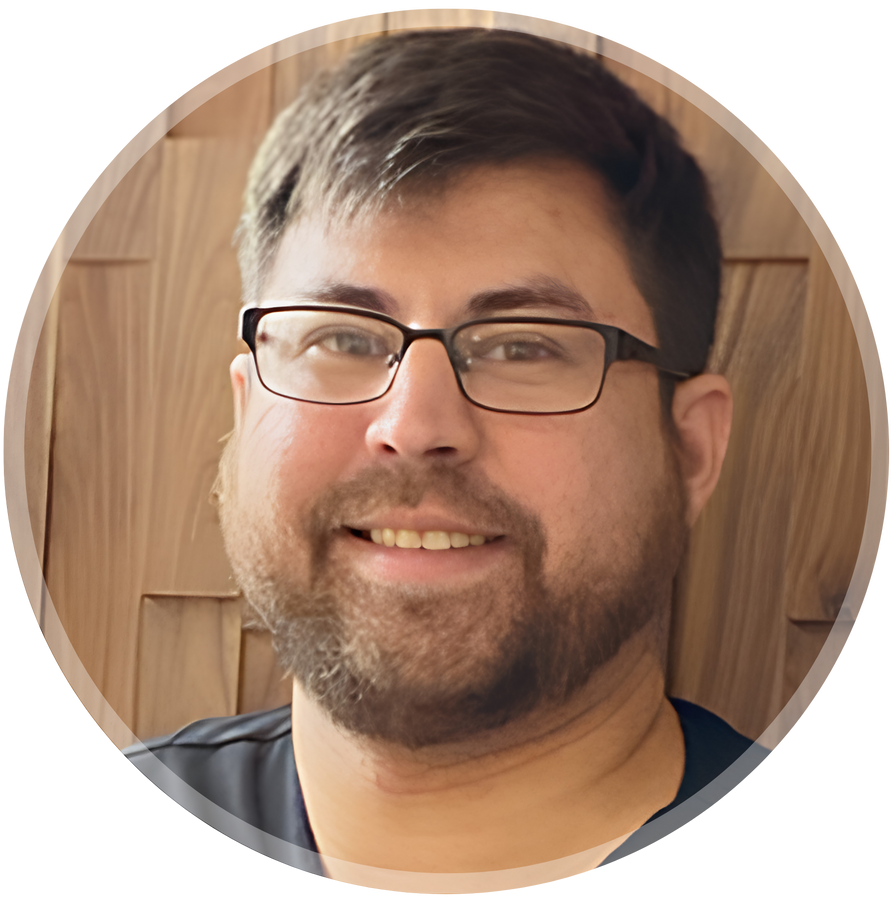 Smiling person with glasses and beard against a wooden background