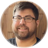 Smiling person with glasses and beard against a wooden background