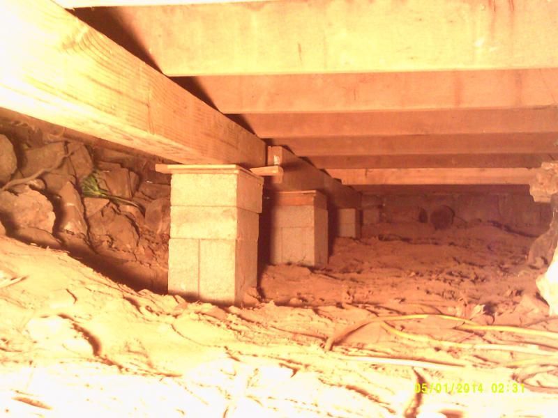 Underneath a house: wood beams supported by concrete block columns in a dirt crawlspace.