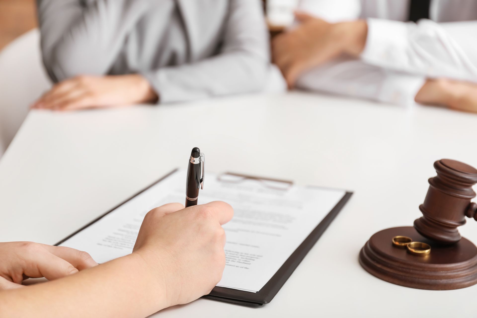 Hand signing a document at a courtroom table beside a judge’s gavel