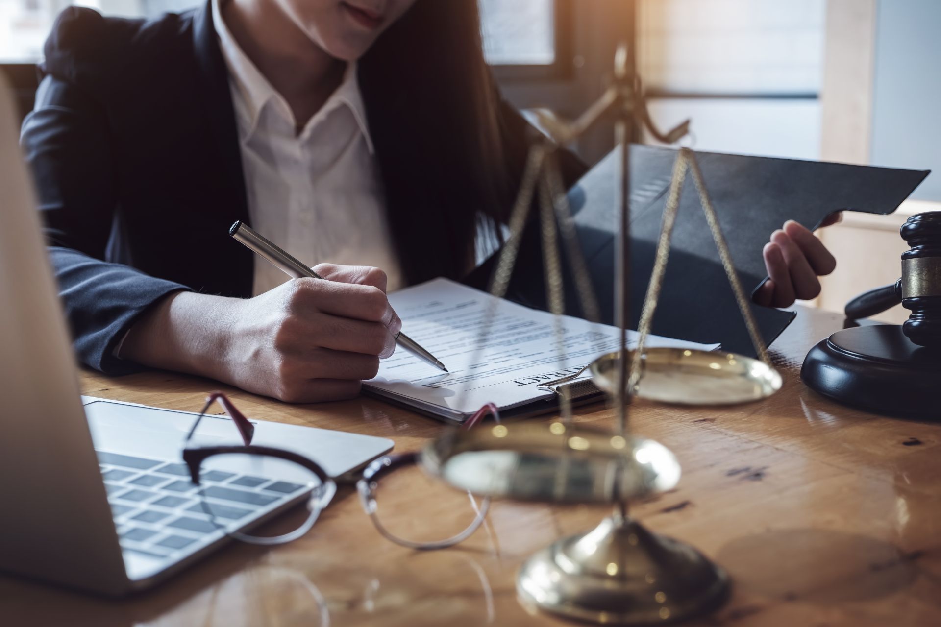 Person writing at a desk with a scales of justice in the foreground and a laptop nearby