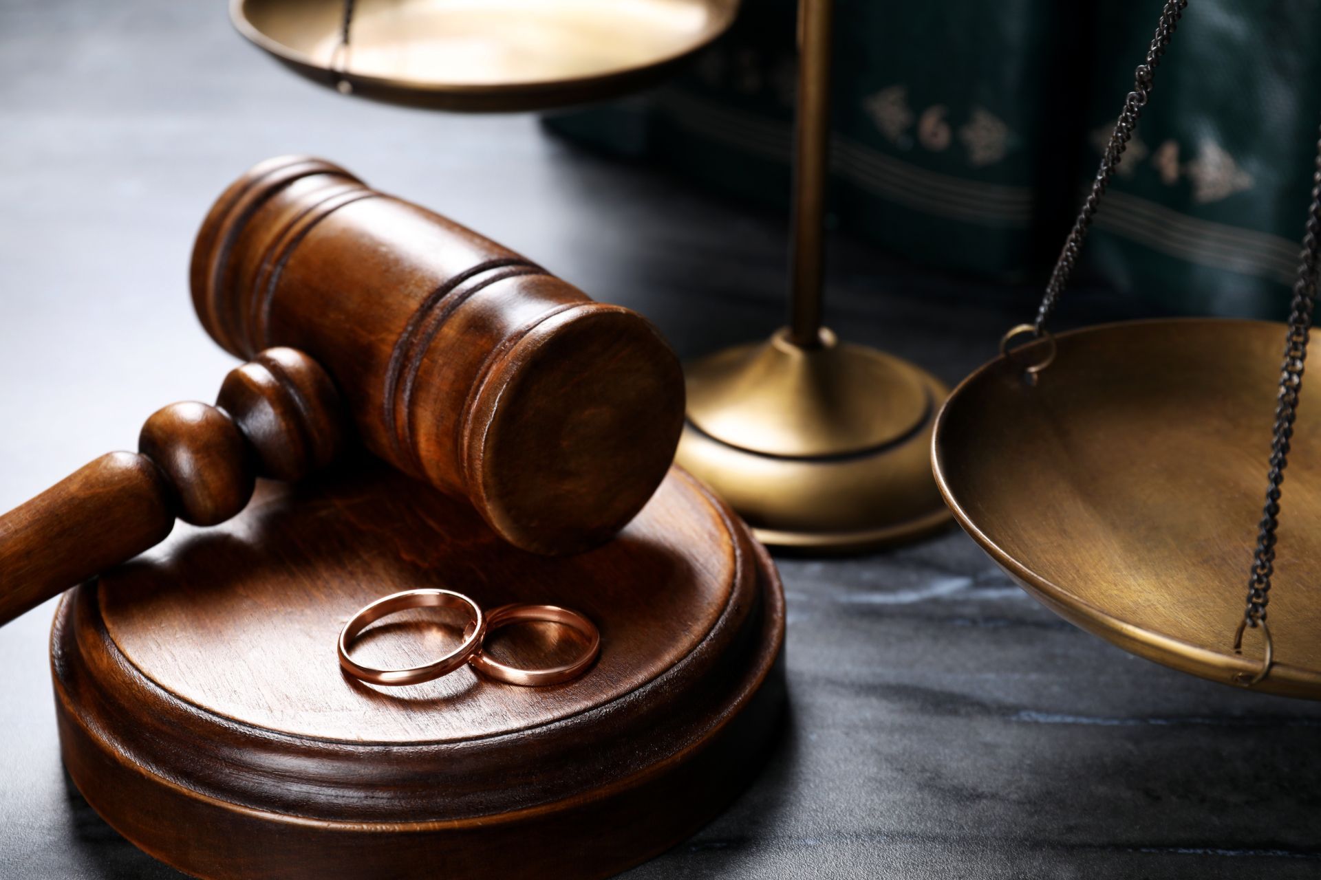 Lawyer’s gavel beside wedding rings on a wooden block, with brass scales in the background