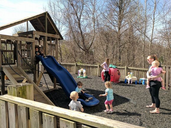 Children playing on a playground slide with adults nearby in a fenced park.