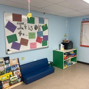 Classroom reading corner with a blue bench, colorful bulletin board, and bookshelves
