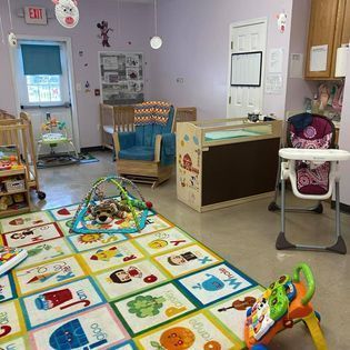 Children's playroom with alphabet rug, toys, and shelves; empty stroller and high chair by the wall.