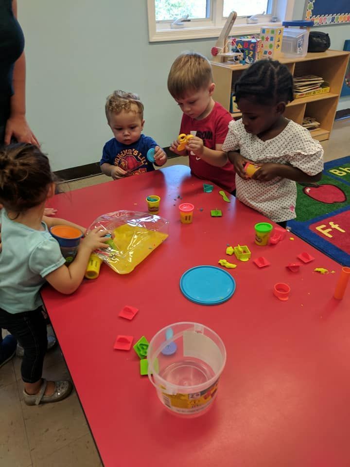 Children playing with colorful blocks at a red table in a classroom.