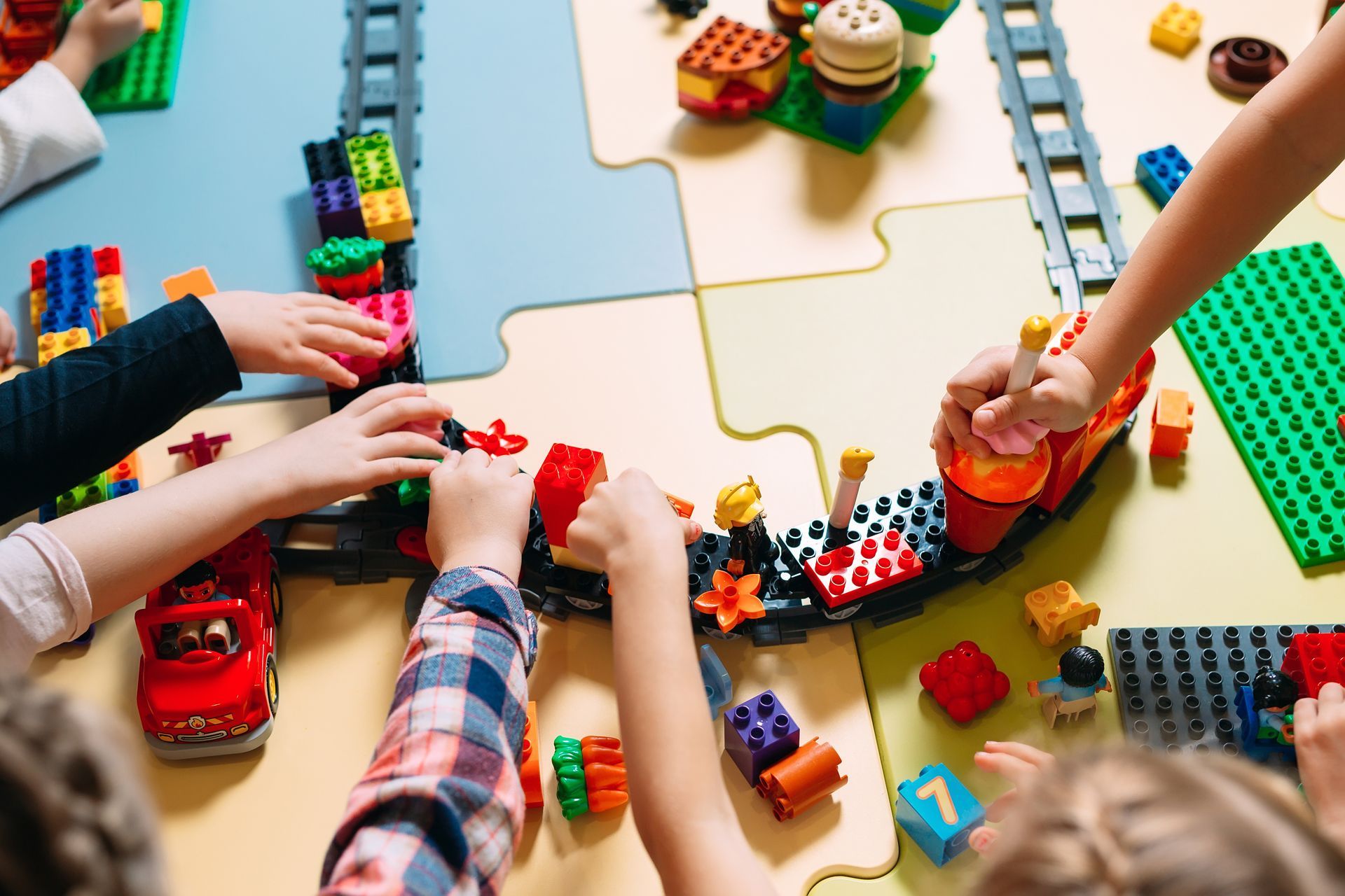 Children playing with toy trains and cars around a curved track on a table