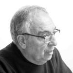 Una fotografía en blanco y negro de un hombre que lleva gafas y una camisa negra.