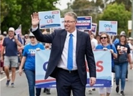 Man in suit waves while walking in a parade;