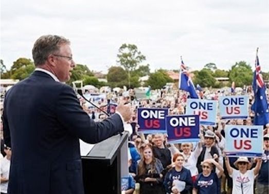 Man speaking at a podium to a crowd holding