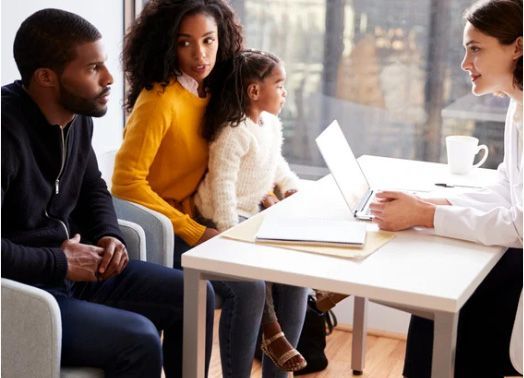 Family, child and consultant seated at a table, discussing documents.