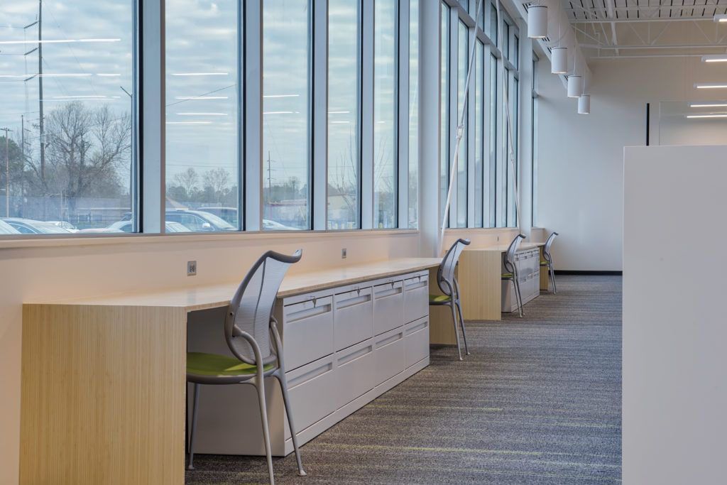 A row of desks and chairs in an office with lots of windows.